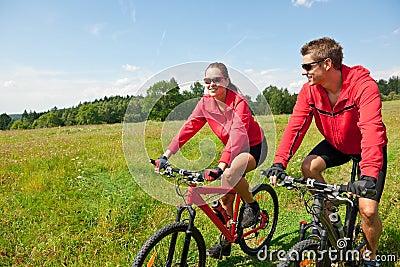 Summer - Sportive couple riding bike in meadow