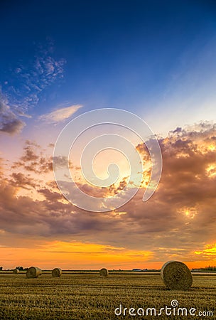 Sunset over farm field with hay bales