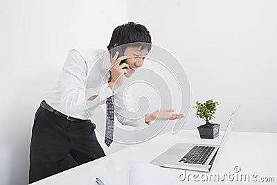 Surprise businessman using cell phone and laptop in office