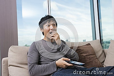 Surprised mid-adult man watching television on sofa at home