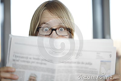 Surprised woman with glasses reading a newspaper