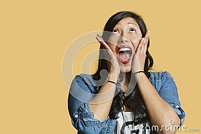 Surprised young woman with head in hands looking up over colored background