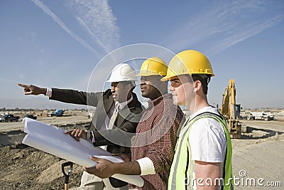Surveyor And Construction Workers With Plans On Site