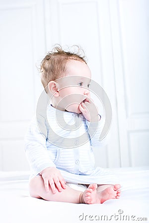 Sweet baby girl sucking on her finger sitting in a white nursery