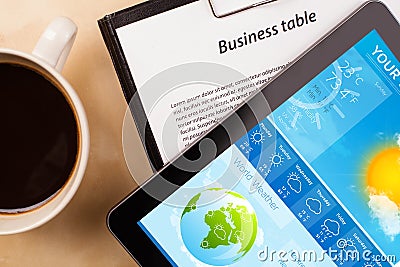 Tablet pc showing weather forecast on screen with a cup of coffe