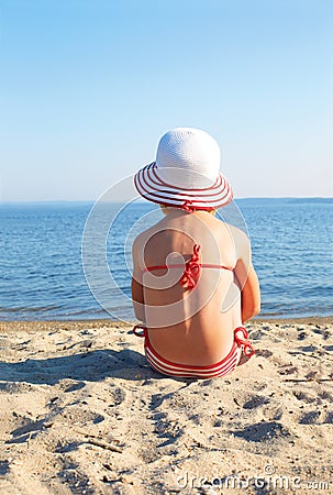 Tanned girl sitting on the beach in white hat