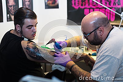 Tattoo master doing tattoo on man arm.