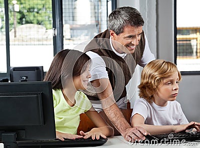 Teacher Assisting Schoolchildren In Using Desktop
