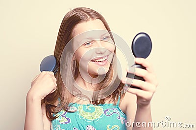 Teen girl holding hairbrush and looking at the mirror