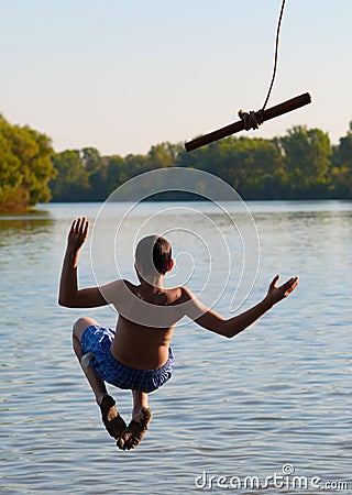 Teenage boy jumping in the river from the rope