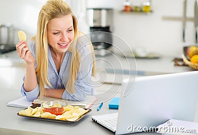 Teenage girl eating chips and looking in laptop