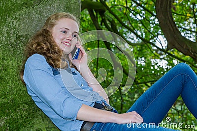 Teenage girl phoning mobile in green tree