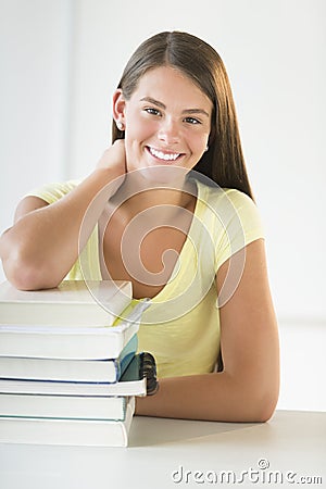 Teenage Student Leaning On Stacked Books At Desk
