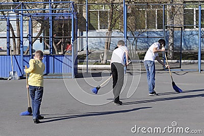 Teenagers sweep the yard with sweepers during a community work d