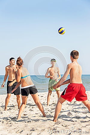 Teenages friends (four people) are playing volleyball on the bea