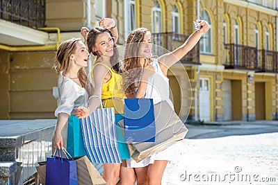 Three girlfriends make selfie on a cell phone. Girls holding sho