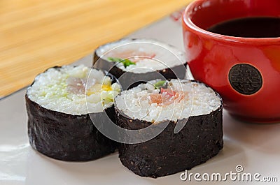 Three sushi rolls with a small bowl of say sauce