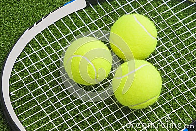 Three tennis balls lie on a tennis racket strings. over green la