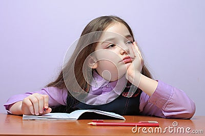 Tired little school girl doing homeworks at desk