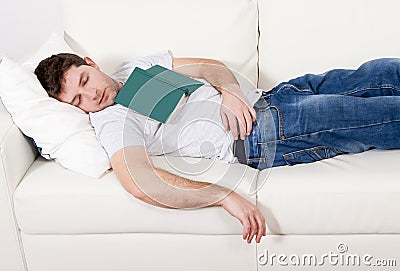 Tired young man sleeping on couch with book on lap