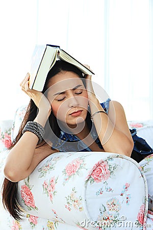 Tired young woman taking a nap at home lying on sofa with a book