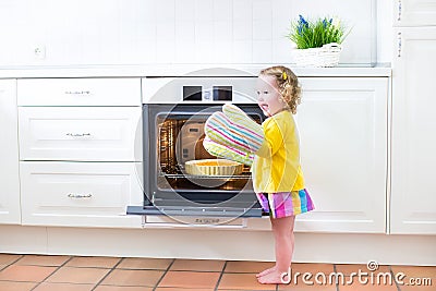 Toddler girl in kitchen mittens next to oven with apple pie