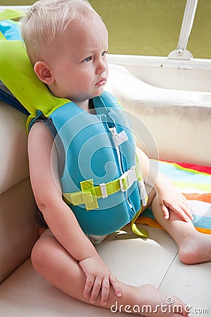 child wearing a life jacket for safety on a boat on a lake.