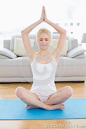 Toned woman sitting with joined hands over head at fitness studio