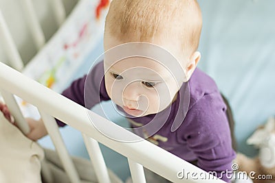 Top view of baby trying to stand up in his cot