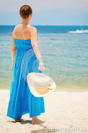 Woman in blue dress throws hat on the beach