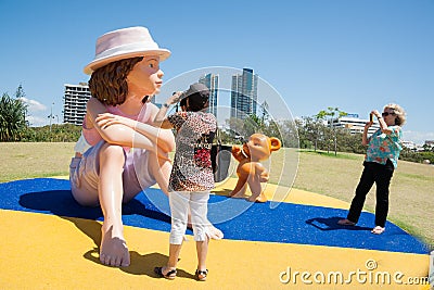 Tourists taking photograph of large model doll and bear.