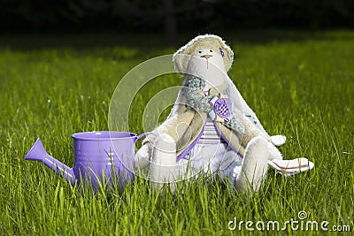 Toy rabbit sitting on grass with watering can