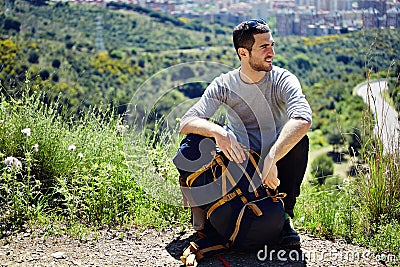 Traveler with rucksack resting on a halt on a mountain trail and looking away