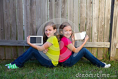 Twin sister girls playing tablet pc sitting on backyard lawn