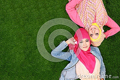 Two beautiful happy muslim woman smiling lying on grass with cop