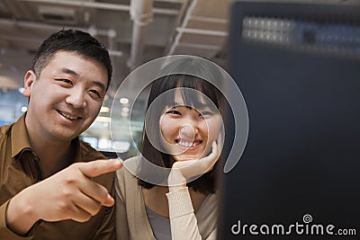 Two Business People Smiling and Looking at Computer in the Office