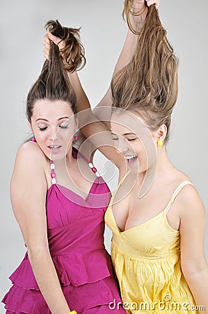 Two funny girl friends pull each other s hair.