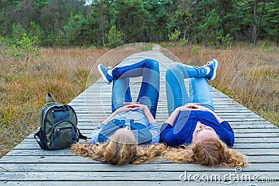Two girls lying on their backs on wooden path in nature
