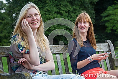 Two girls sitting on bench in park with mobile