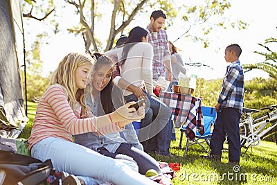 Two Girls Using Mobile Phone On Family Camping Holiday