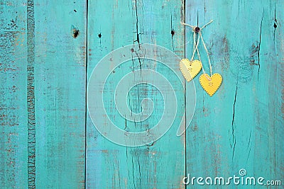 Two gold hearts hanging on antique teal blue wood fence