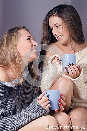 Two happy girlfriends drinking tea or coffee together