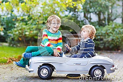 Two happy kids playing with big old toy car in summer garden, ou