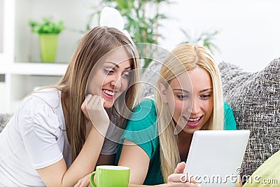 Two happy young women with digital tablet relaxing in room