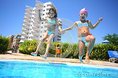 Two little girls holding hands fun jumping into the swimming pool