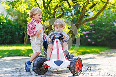 Two little sibling boys playing with pedal car in home s garden