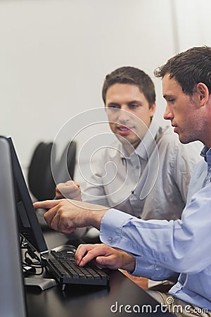 Two mature men talking while sitting in front of computer