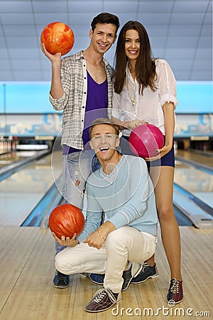 Two men and girl hold balls in bowling club