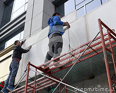 Two men stand on scaffolding and work