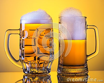 Two Mugs of fresh beer with cap of foam, on yellow back